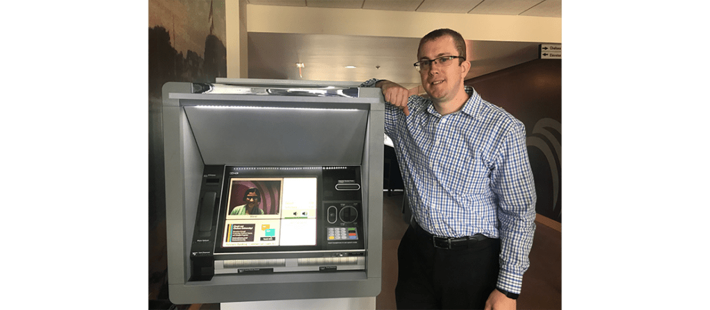 Bill Mundell smiling and resting his arm on an ATM