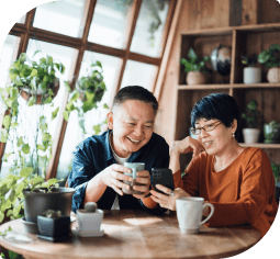 A smiling Asian couple with mugs look at a smart phone