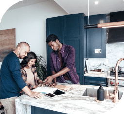 Three people look at paper work around a kitchen island