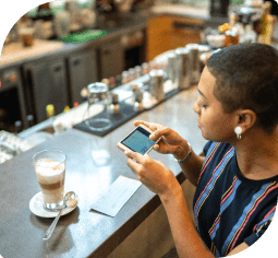 A woman at a bar counter uses a mobile device to scan a check