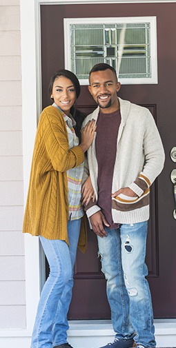 A full body portrait of a smiling woman and man on a front porch