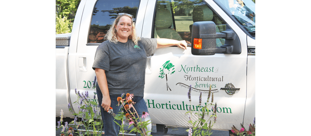 Stacey Marcell rests her hand on a white truck with text that reads "Northeast Horticultural Services"