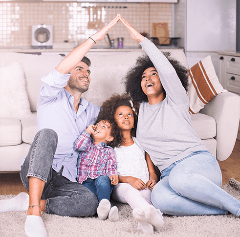 A man and women sitting on the ground of a living room touch finger tips above the heads of two young children sitting on the ground