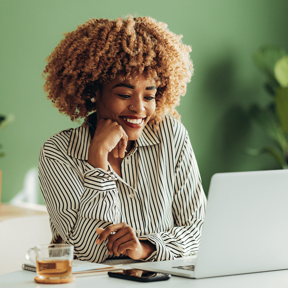 A woman smiles while looking down at her laptop