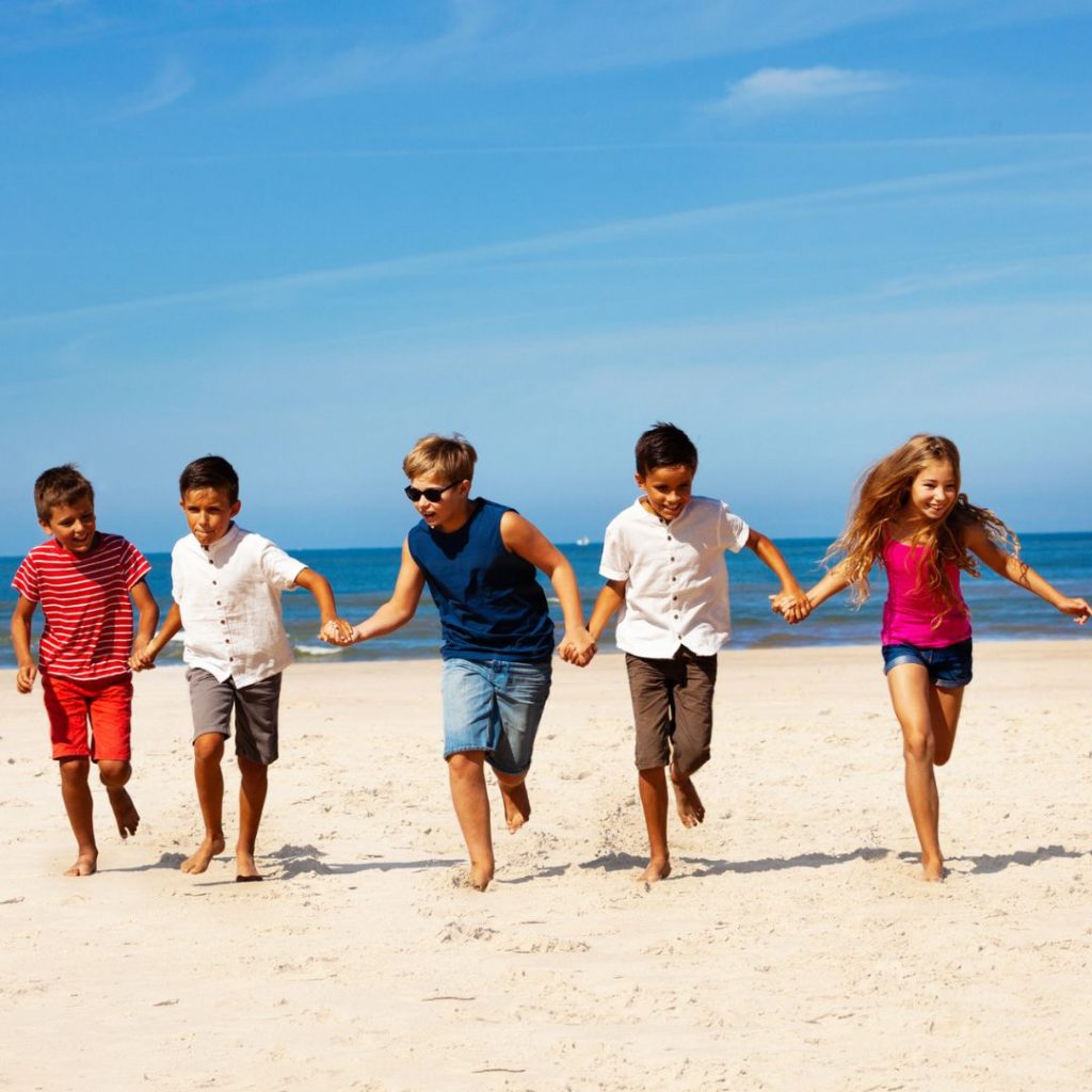 Kids running on a beach during summer.
